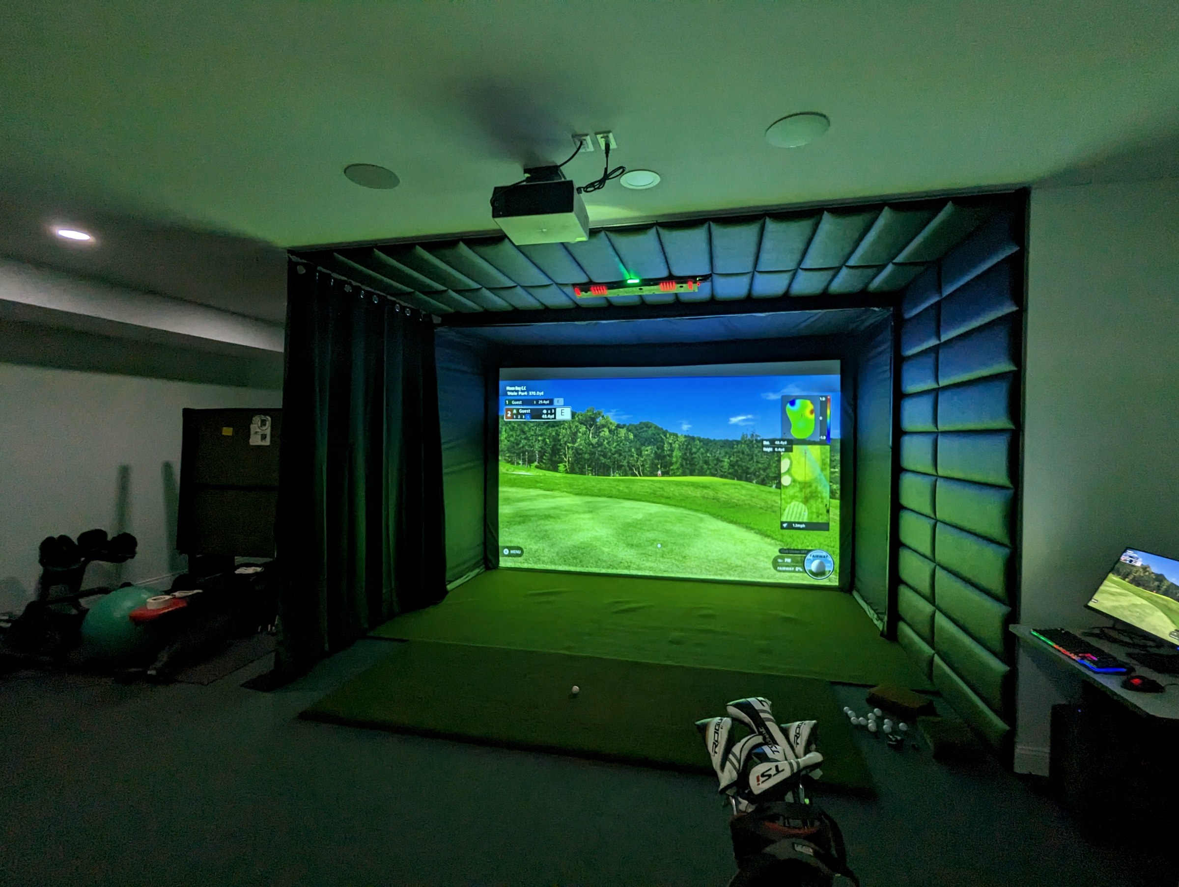 Wide view of a complete indoor golf simulator bay and equipment area